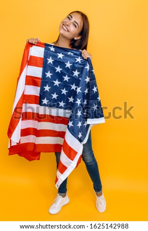 American dream. Young beautiful girl in a white t-shirt with the American flag, on a yellow background.