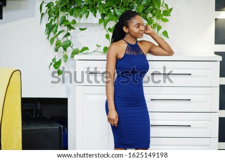 Charming african american woman in blue dress posing at restaurant.