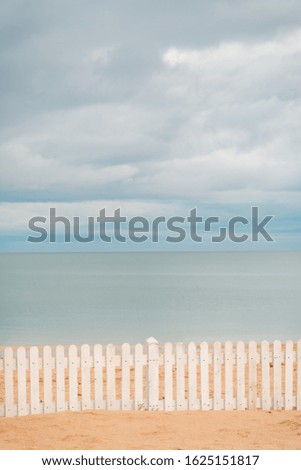 Wooden Fence in Sand on Beach. View of a white wooden fence standing on a sandy beach and the sea in the background. 