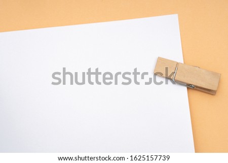 White paper on orange background held by wooden clothes-pegs