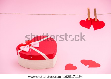 Heart shaped gift box and red paper hearts on pink pastel background. Clothes pegs and red paper hearts on rope. Valentines day concept