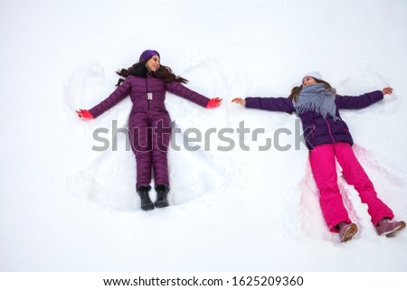 Snow Angels. Two Young beautiful girls in a ski suit lies on the snow, top view