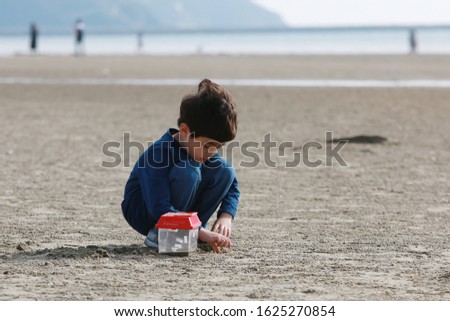 Against the backdrop of beach sand, a boy dressed in navy blue is looking for shellfish hidden in the sand with his hands. Out Focus picture.