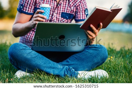 Campus life. Student working with laptop and reading a book while learning in the park, close up photo. Education, lifestyle concept