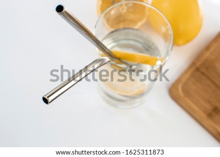 Reusable Metal Straws with Portable Case - Stainless Steel, Eco-Friendly Drinking Straw Set with  Cleaning Brushes. A glass of water with a metal drinking straw. Yellow lemons on a white background. Royalty-Free Stock Photo #1625311873
