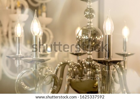 The picture of a glowing chandelier with metal chrome fixtures and shades in the form of candles. The concept of the classical style in the interior. Close up. Soft warm filter, selective focus.