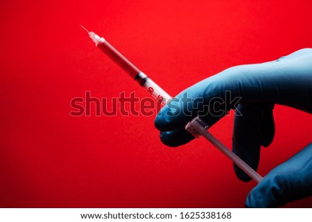 Doctor holding medical syringe on red background