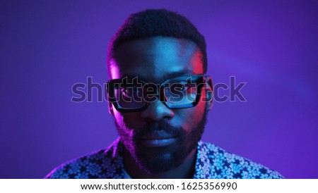 Portrait of handsome young African American male dressed in flowered shirt looking at camera with serious and confident expression on his face in neon lights. People and lifestyle concept. Male studio
