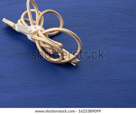 twisted golden cable for charging with electricity equipment in textile winding on a blue wooden background, close up