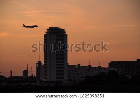 A silhouetted airplane landing at London City Airport, against the orange glow of sunset. 