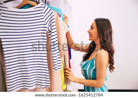Dressing for the party. Close-up photo of a charming girl in a casual outfit, who is choosing what to wear from a great number of items of clothing in her wardrobe.