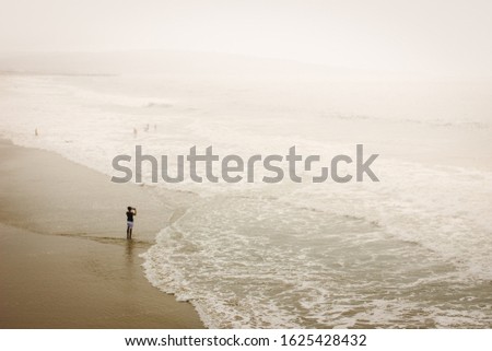 A lone traveler taking a picture of the Pacific Ocean at Hermosa Beach in California on a misty morning.