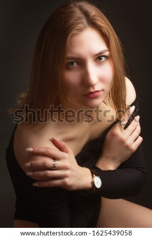 Portrait in the photo Studio of a brown-haired girl, on a black background in black clothes with open shoulders. Short hair.