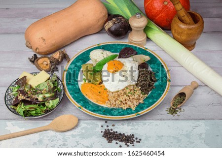 Vegetarian dish served with a small plate of salad. Decoration with vegetables. Served on a pretty plate on a wooden table, with wooden spoons.