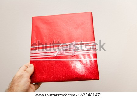 Man hand holding against white background beautifully packaged red gift present whit white bands for the upcoming birthday valentine new year christmas Hanukkah black friday holiday