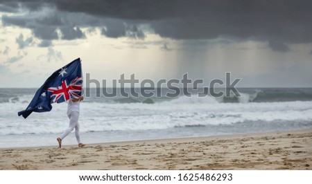 Australian flag blowing in the wind held by a female jogging seaside on a Aussie beach, with dramatic storm clouds background. Australia day flag and waiting for rain concepts Royalty-Free Stock Photo #1625486293