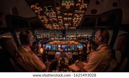 Flight Deck of a modern commercial jet transport aircraft during night cruise. Cozy airliner cockpit atmosphere generated by warm avionic instrument lights and Europe cityscapes in the horizon Royalty-Free Stock Photo #1625493028