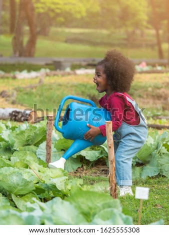 Vertical picture, cute little African girl carrying huge watering can water vegetable in the garden.  Children happiness spending quality time with family in the park.