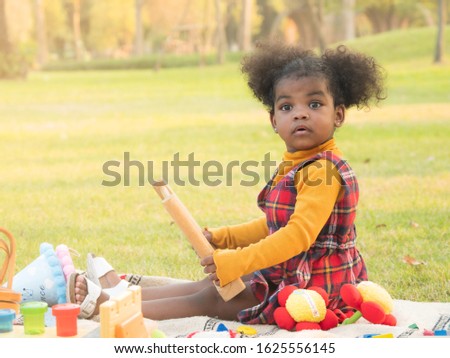 Adorable little African girl looking very curious or surprise while playing with toys during picnic in the park.