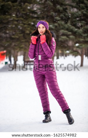Full-length portrait of a young beautiful brunette girl in a ski suit posing in winter park