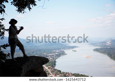 Thai woman travel visit and posing take photo on ridge stone of cliffs at Wat Pha Tak Suea temple with view of landscape of Nongkhai city and loas and Mekong river in Nong Khai, Thailand