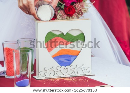 A picture in the form of a heart filled with colorful sand is on the table. Sand ceremony at the wedding. Holiday concept - Valentine's day, family day, wedding.