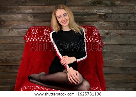Portrait of a pretty young blonde woman with minimal makeup in a sports dress on a wooden background. Sits on a red sofa opposite the camera in various poses.