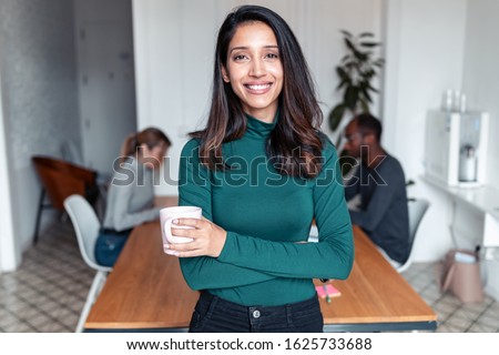 Shot of young indian business woman entrepreneur looking at camera in the office. In the background, her colleagues working. Royalty-Free Stock Photo #1625733688