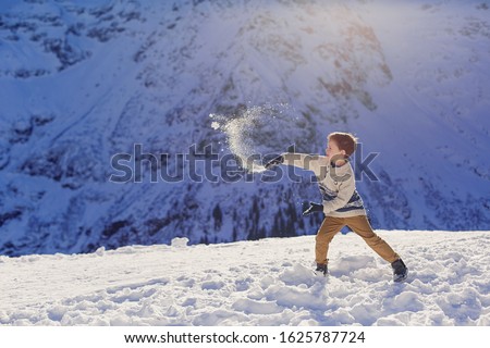 Child boy 5 years in a winter sweater plays snowballs in the mountains. Snow peaks on background. Beautiful landscape of the Alps. Ski resort. Children's game fun vacation holidays leisure. Childhood