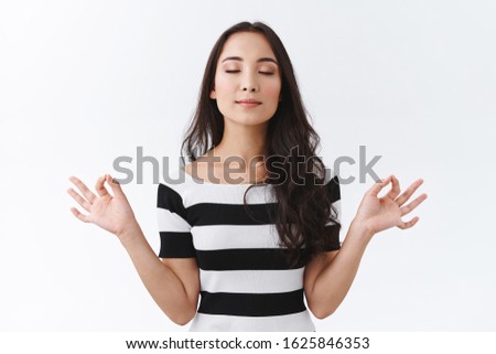Portrait of calm and relieved east-asian woman keep mind healthy, relaxing with yoga or meditating practice, deep breath and close eyes, hold hands sideways with mudra zen signs, white background