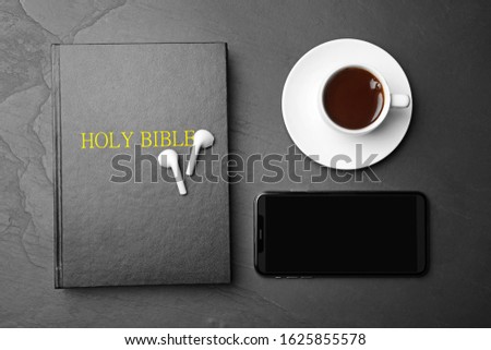 Bible, phone, cup of coffee and earphones on black background, flat lay. Religious audiobook