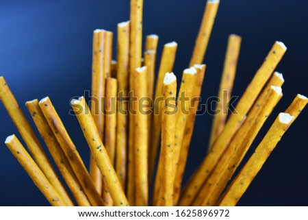 Tasty and sweet straws with poppy seeds made of flour, sneking scattered on a black plastic background.