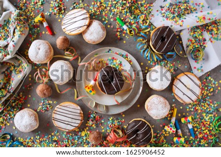 Sweet mardi gras donuts decorated on a gray table with colorful confetti and streamers. Flat lay Photography. 
Top view for a mardi gras background.