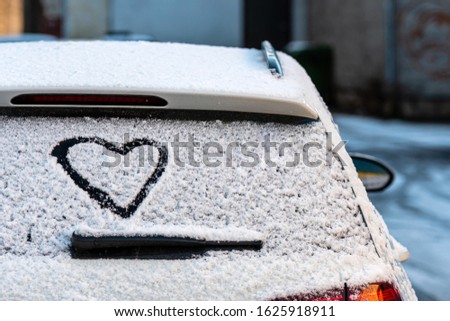 Heart shape on snow covered car rear window, close-up