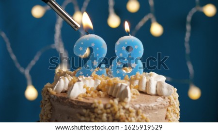 Birthday cake with 28 number candle on blue backgraund set on fire by lighter. Close-up view