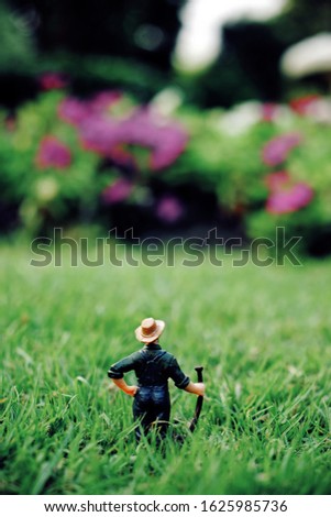 Back view of miniature farmer man standing at Nature flower garden, vertical picture   