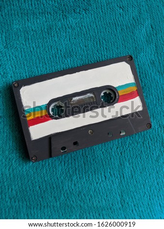 Unique, Hand Painted cassette tape in white, teal, orange, and red on a velvety blue background capturing the heart of aspiring artists making new waves with old things and embodying history of past.
