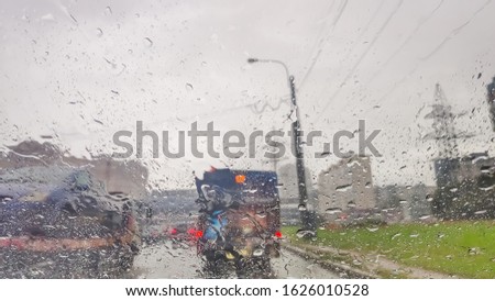 Background is blurred, raindrops on the windscreen to car. Water droplets on the glass surface on the road. Blur, bokeh and street lights behind.heavy rainy and slippery road. Abstract bad weather car