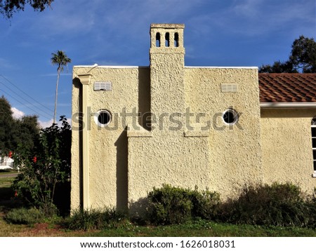 Stucco house with chimney and round windows, blue sky in background. 