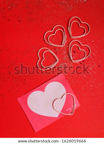The flat lay and top of the clips in the shape of the heart on the red background with  glitter and the copy space. Valentine's day concept, love, romantic.