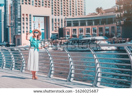 Happy asian girl taking selfie photo on a smartphone while walking on a promenade in Dubai Marina district. Travel and lifestyle in United Arab Emirates