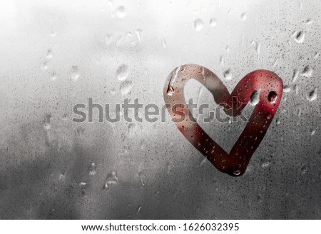 Red heart painted on glass in Rainy weather, is fogged up and there are many drops on it, and the sun shines outside the window at dusk, banner with copy space, Valentine's Day concept