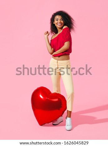 Happy girl with red heart shape balloon. Photo of smiling young girl in love on pink background. Valentine's Day