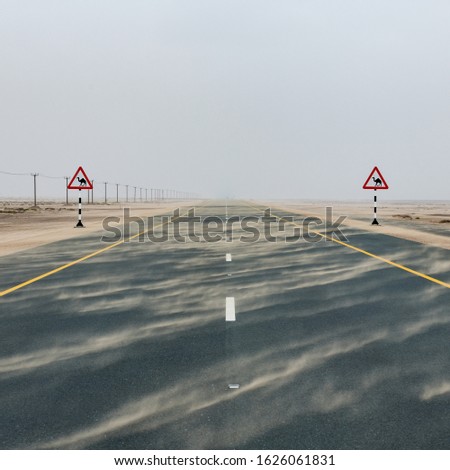 Highway road among desert during sand storm with road signs with camel warning