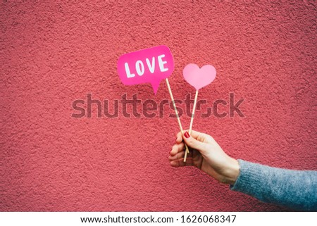 Valentine's Day in February. In a female hand, paper flags of love on sticks on a pink background.