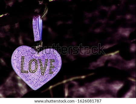 A delicate lilac heart with the inscription love on an abstract blurred dark background.