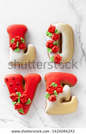 Love sign made of gingerbread cookies with red icing on the white marble background. St. Valentine's day.