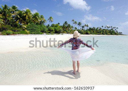 Rear view of young happy woman enjoys the serenity of a deserted tropical island in Aitutaki Lagoon, Cook Islands. Concept photo of women freedom, travel, vacation, happiness, solo, alone, single, fun