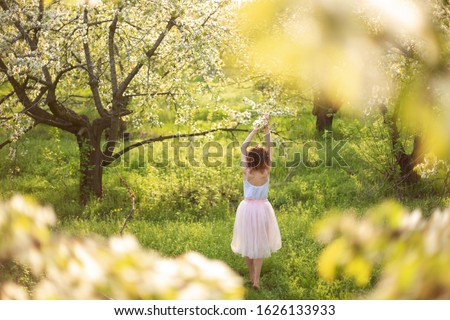 Young attractive girl walks in spring green park enjoying flowering nature.