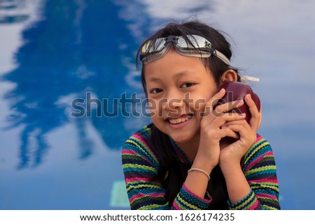 Asian little girl holding apple at the swimming pool with wear swimming goggles